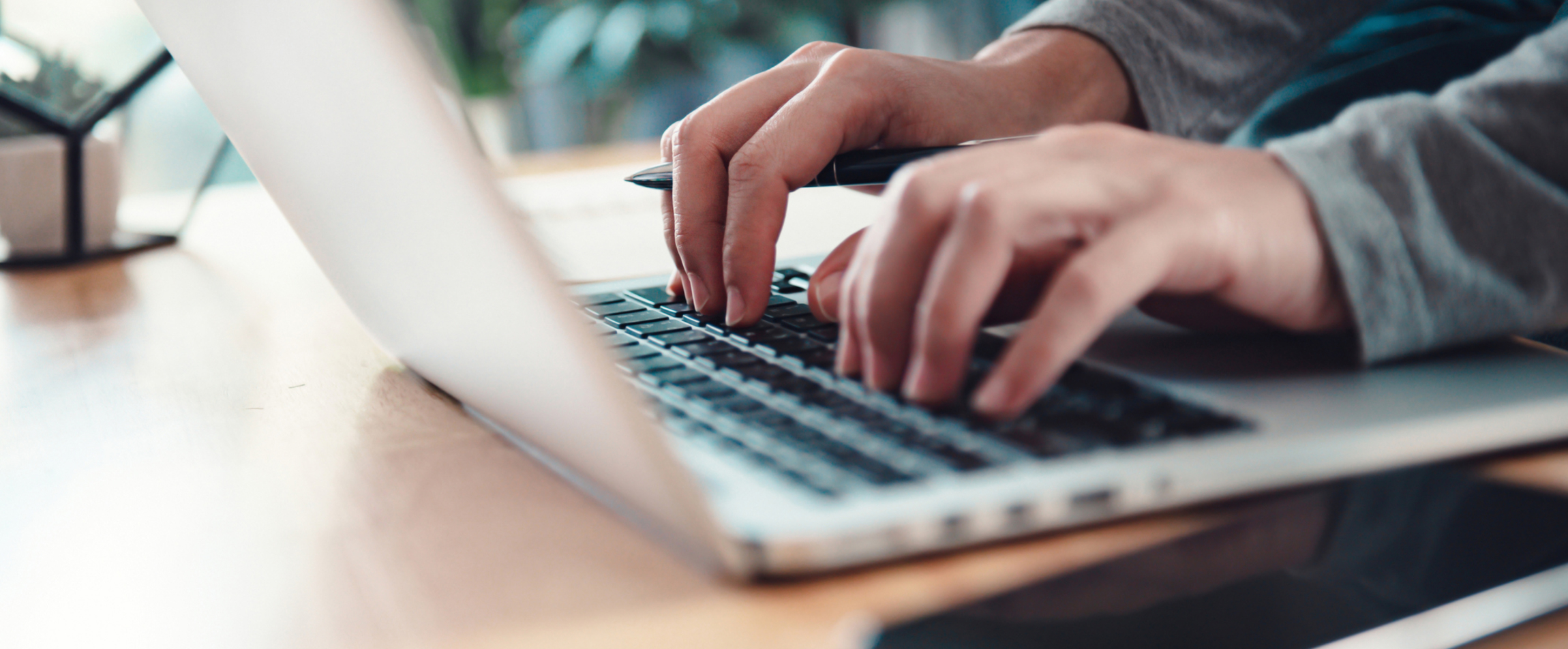 Een persoon typt op een laptop aan een bureau