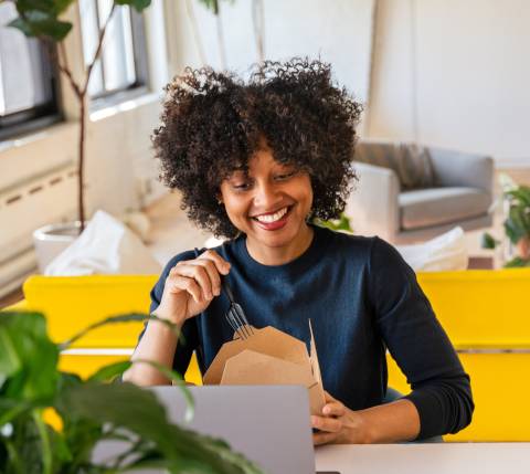 Woman eating takeout in front of laptop