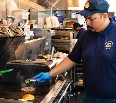 A cook in The Melt kitchen grilling a burger