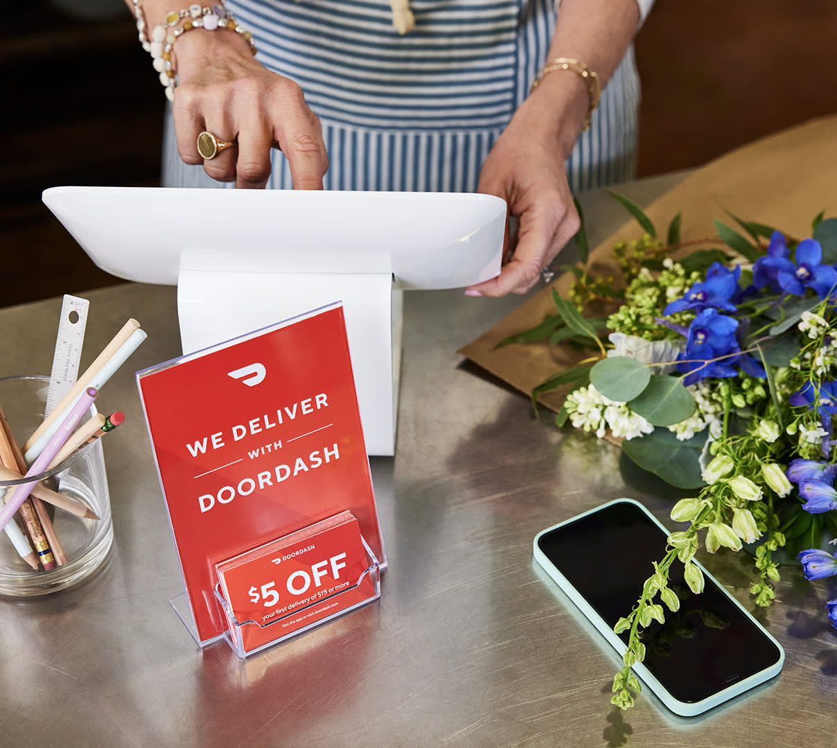 Small business counter with POS and phone with DoorDash coupons and flowers