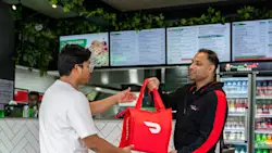 Manoosh Pizzeria employee hands a Dasher a DoorDash bag