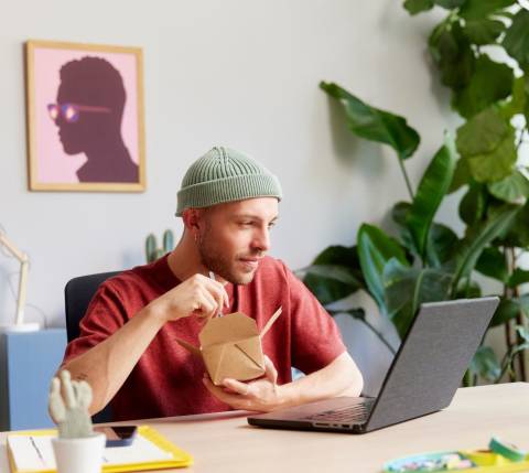 DDfB Man eating noodles in front of computer