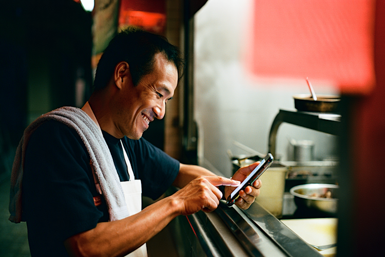 Restaurant worker smiling while looking at a phone in a kitchen with red lighting