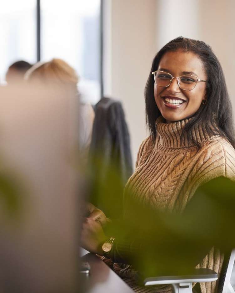 woman in glasses smiles from her office desk