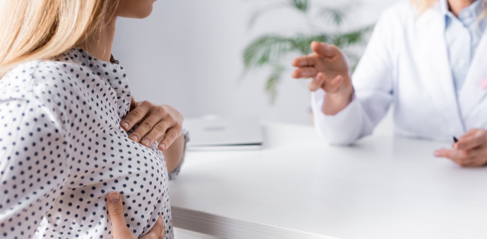 Paciente joven tocando sus senos frente a una doctora que le explica sus síntomas