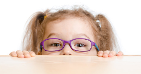 girl with glasses peeking over a desk
