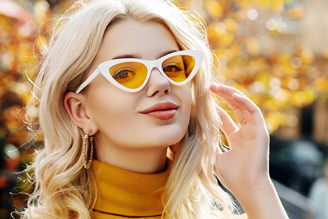 Woman wearing yellow lenses and white framed cat-eye sunglasses outdoors in autumn
