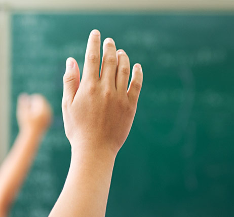 Child raising hand in front of a blurry chalkboard