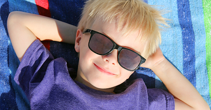 boy laying on beach towel wearing sunglasses