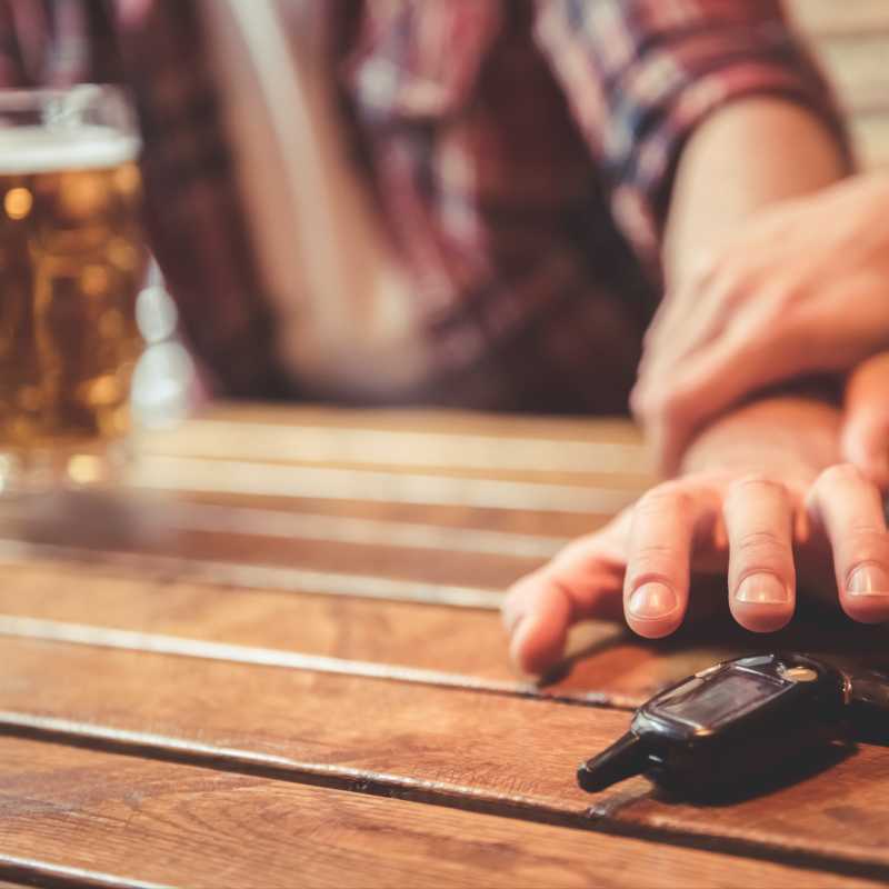 Ein Mann, vor dem ein Bierglas steht, möchte nach seinem Autoschlüssel greifen. Ein Freund hält ihn zurück.