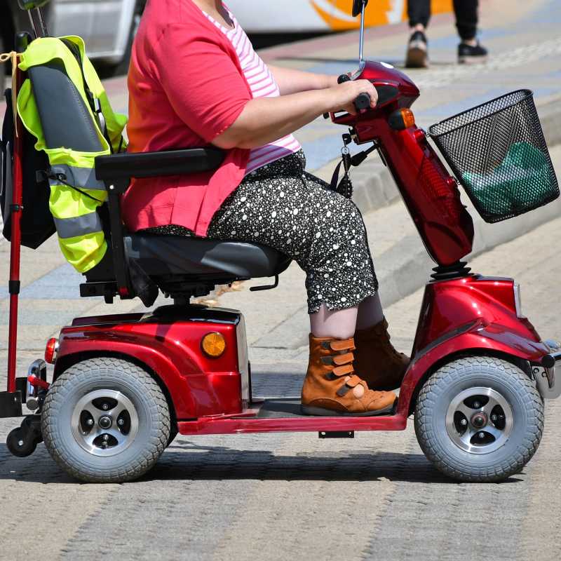 Eine Frau fährt mit einem motorisierten Krankenfahrstuhl in einem verkehrsberuhigten Bereich.
