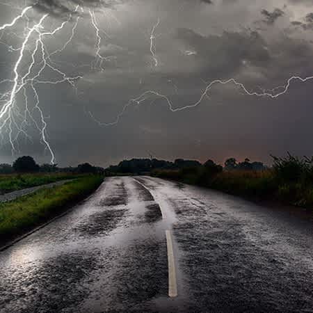 Ein Blitz schlägt im Hintergrund einer Landstraße ein.