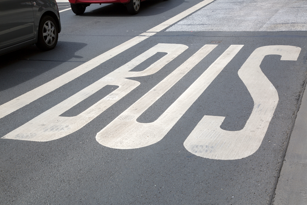 Nahaufnahme einer Fahrbahnmarkierung mit dem Schriftzug „BUS“ auf einer asphaltierten Busspur.