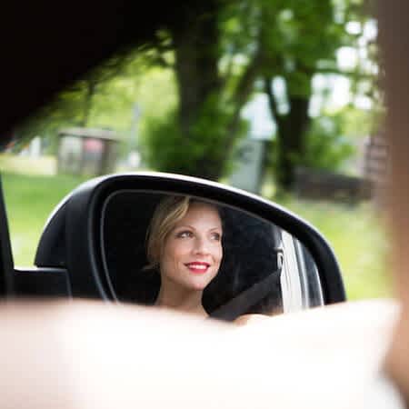 Nina Wortmann sitzt in einem Auto auf dem Beifahrersitz, man sieht sie im Seitenspiegel lächeln.