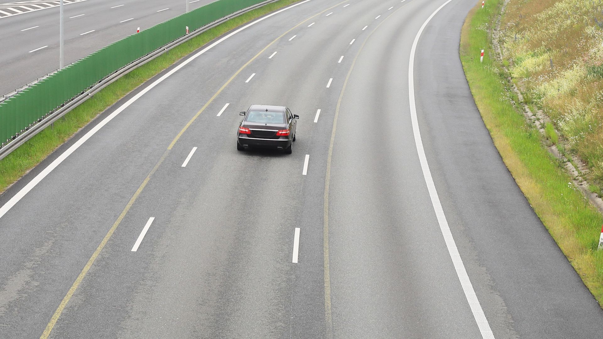 Ein schwarzer Pkw fährt auf der mittleren Spur einer Autobahn, die rechte Spur ist frei.