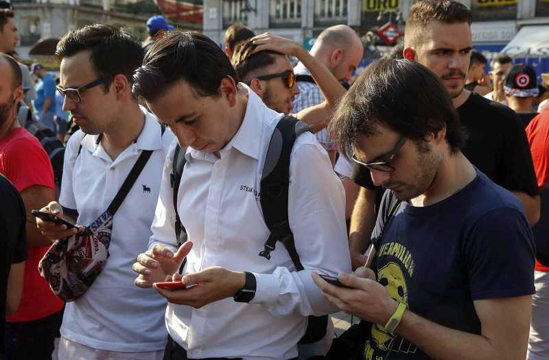 In einer Traube von Menschen schauen drei Männer auf ihr Smartphone.