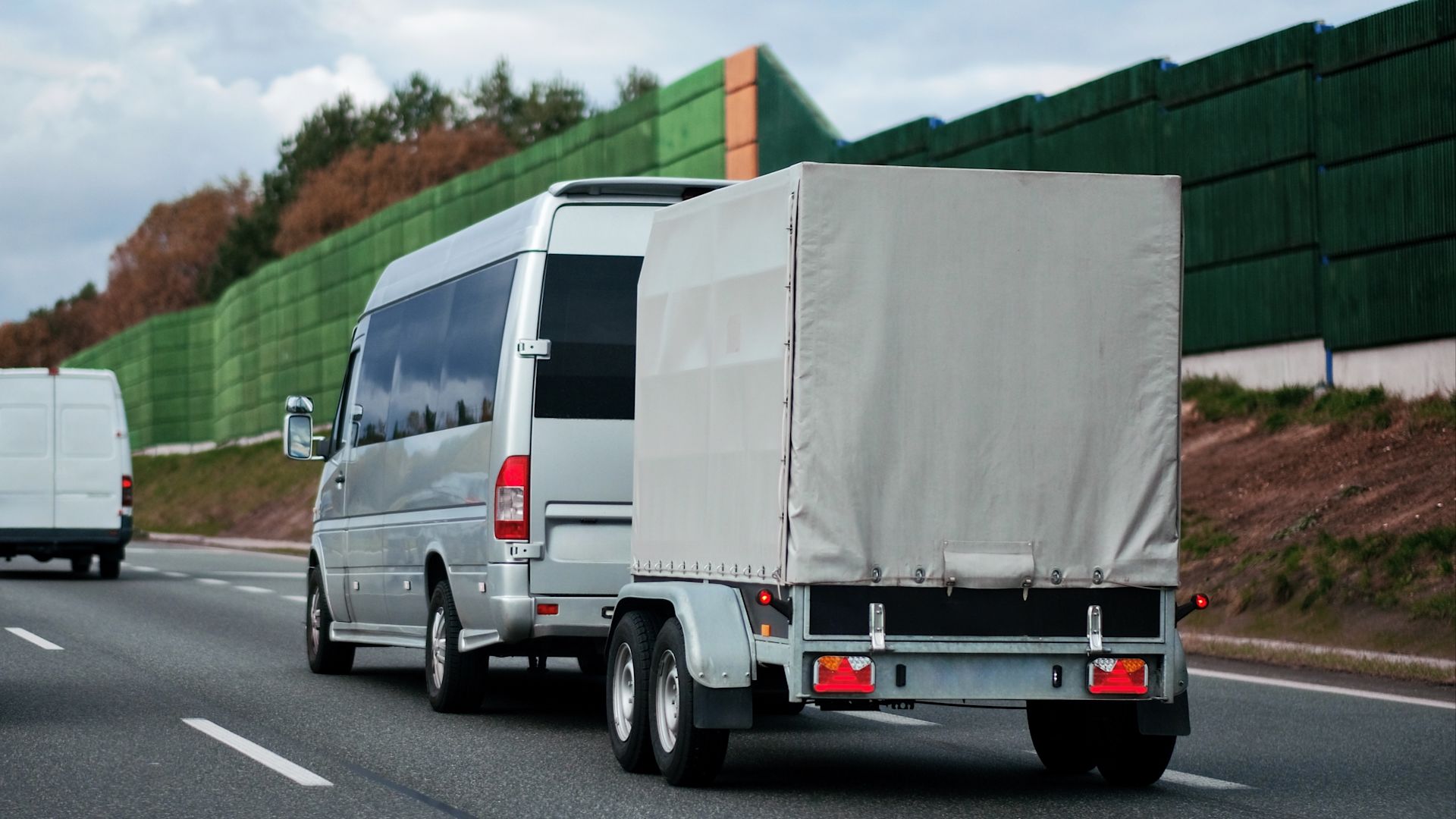 Ein kleiner Transporter zieht einen Anhänger mit Plane auf der Autobahn.