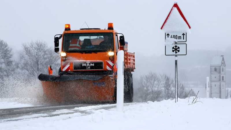 Ein Räum- und Streufahrzeug fährt eine verschneite Landstraße entlang und räumt den Schnee.