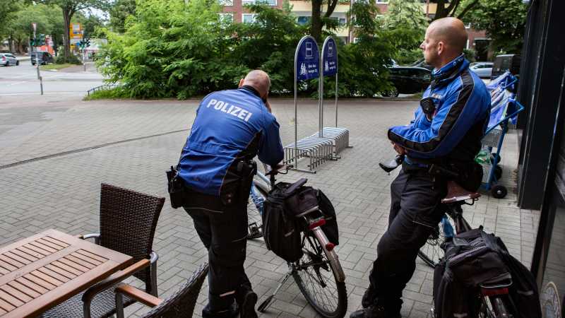 zwei Fahrradpolizisten stehen neben ihren Fahrrädern und beobachten eine Kreuzung. 