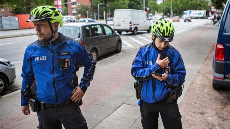 Die Fahrradpolizisten Jens Cissek und Sabrina Friedrich stehen an einer Seite einer Straße und unterhalten sich über Funk.
