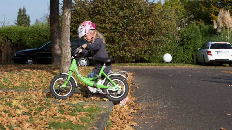 Ein kleines Mädchen schiebt ein Fahrrad über eine Bordsteinkante.