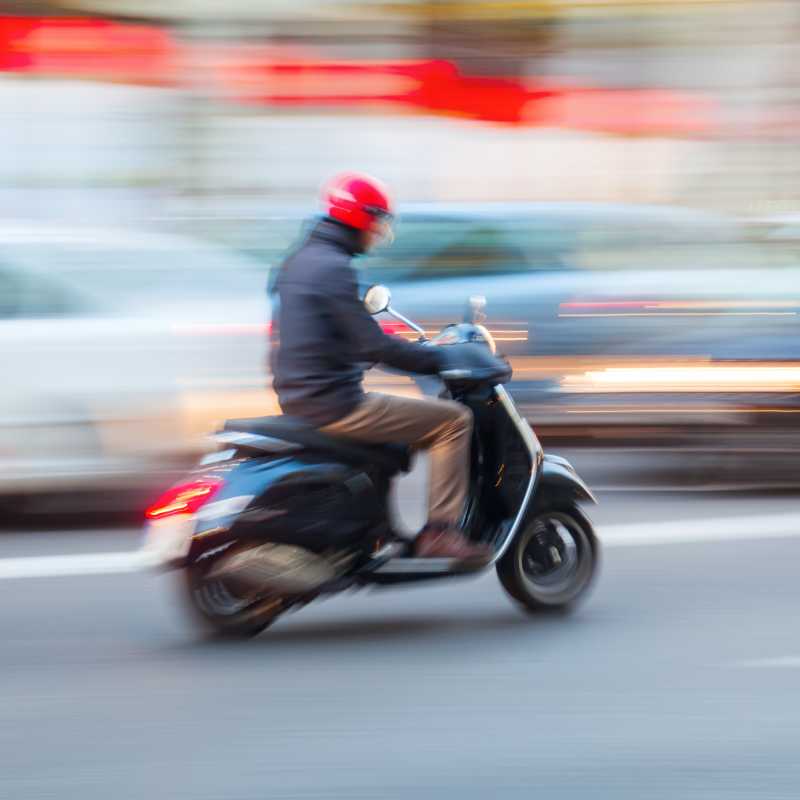Ein Mann fährt auf einem Motorroller durch den lebendigen Straßenverkehr. 