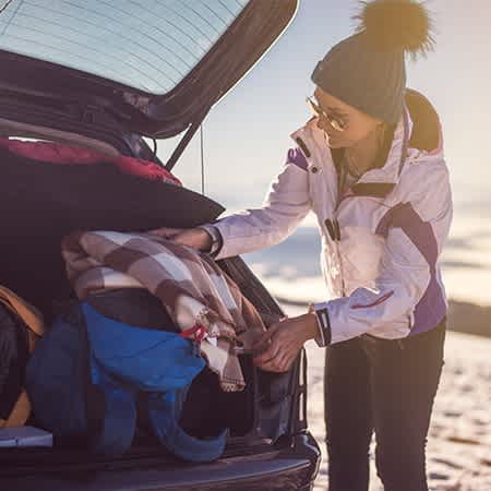 Eine Frau verstaut ihre Skiausrüstung im Kofferraum eines Autos.