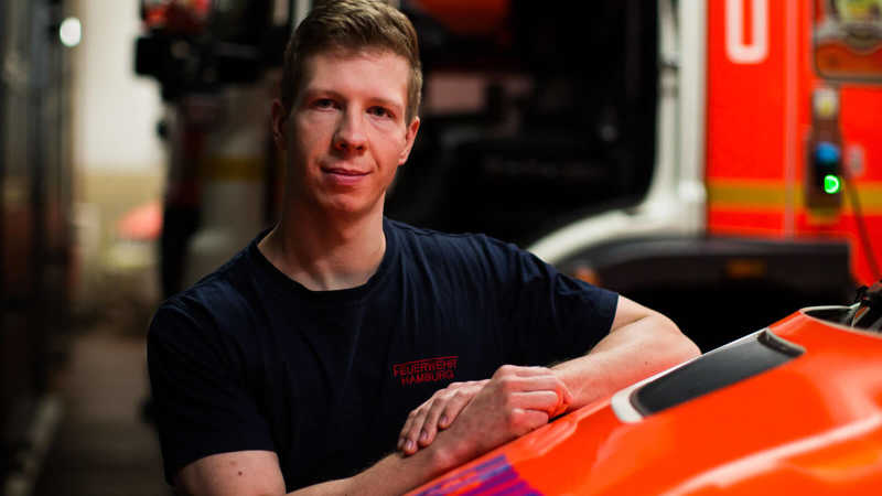 Das Bild zeigt einen Feuerwehrmann angelehnt an ein Feuerwehrfahrzeug.