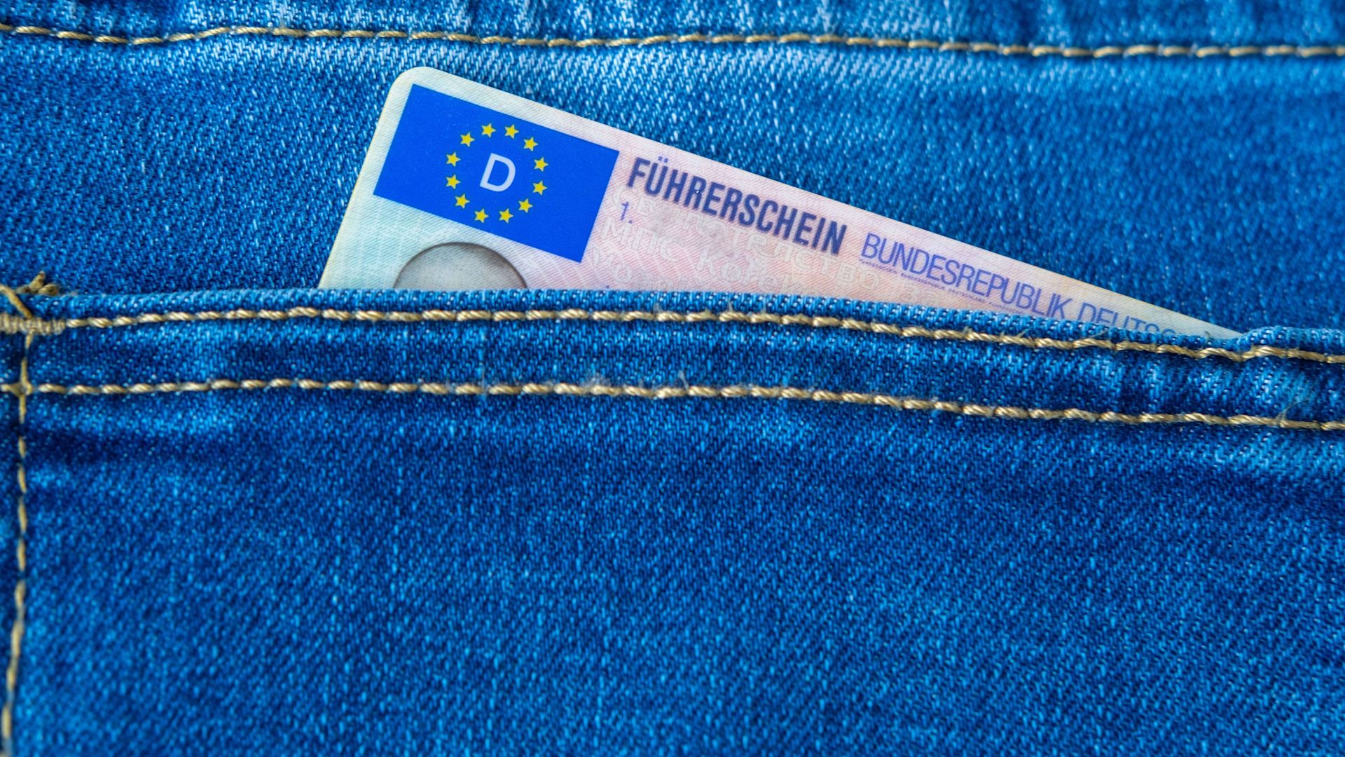 Nahaufnahme eines Führerscheins der Bundesrepublik Deutschland, der aus einer Taschenöffnung einer Jeanshose ragt.
