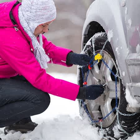 Eine Frau legt Schneeketten an ihrem Auto an.