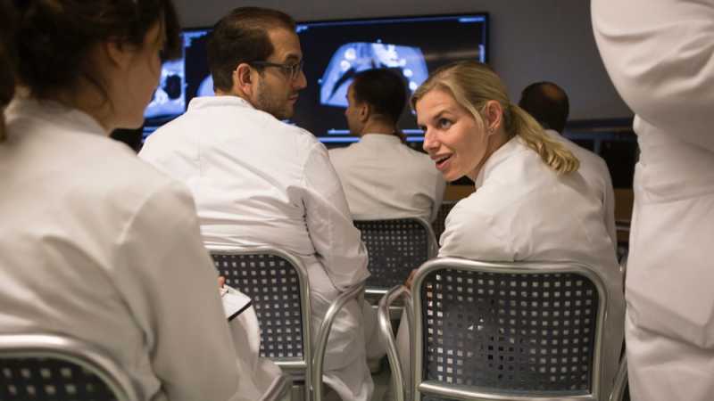 Das Bild zeigt eine junge Ärztin in einer Besprechung mit Kollegen und Kolleginnen.