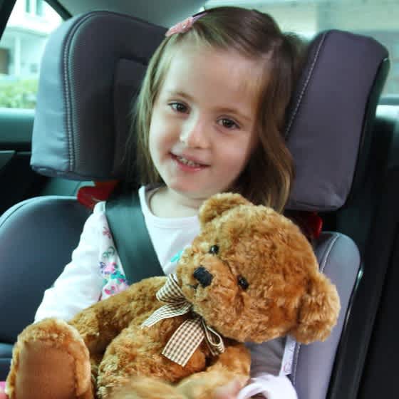 Ein Mädchen mit Teddybär in den Armen sitzt in einem Kindersitz in einem Auto.