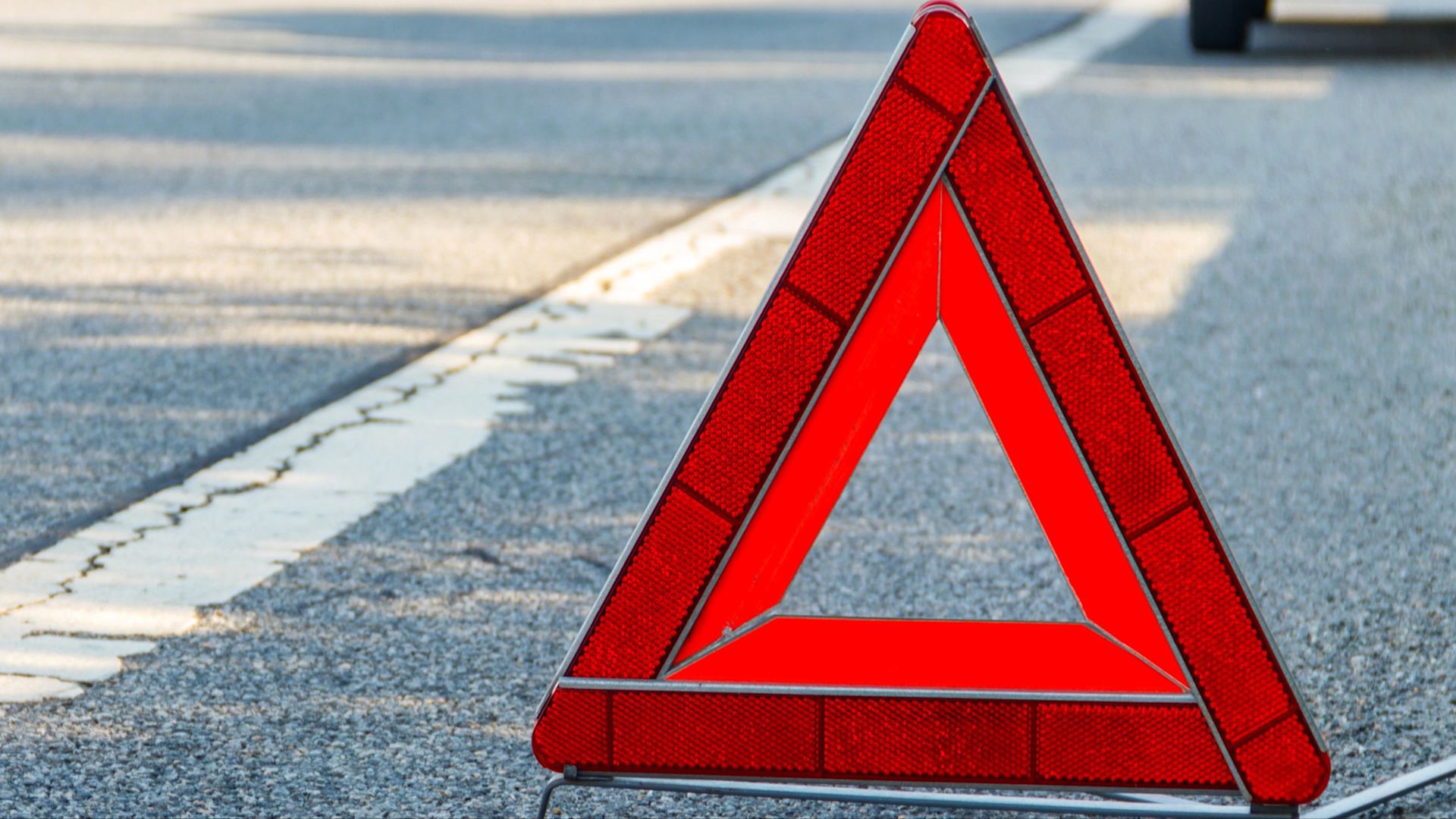 Rotes Warndreieck auf dem Asphalt am Seitenstreifen. Das Warndreieck sichert eine Pannen- oder Unfallstelle ab und warnt den Verkehr.