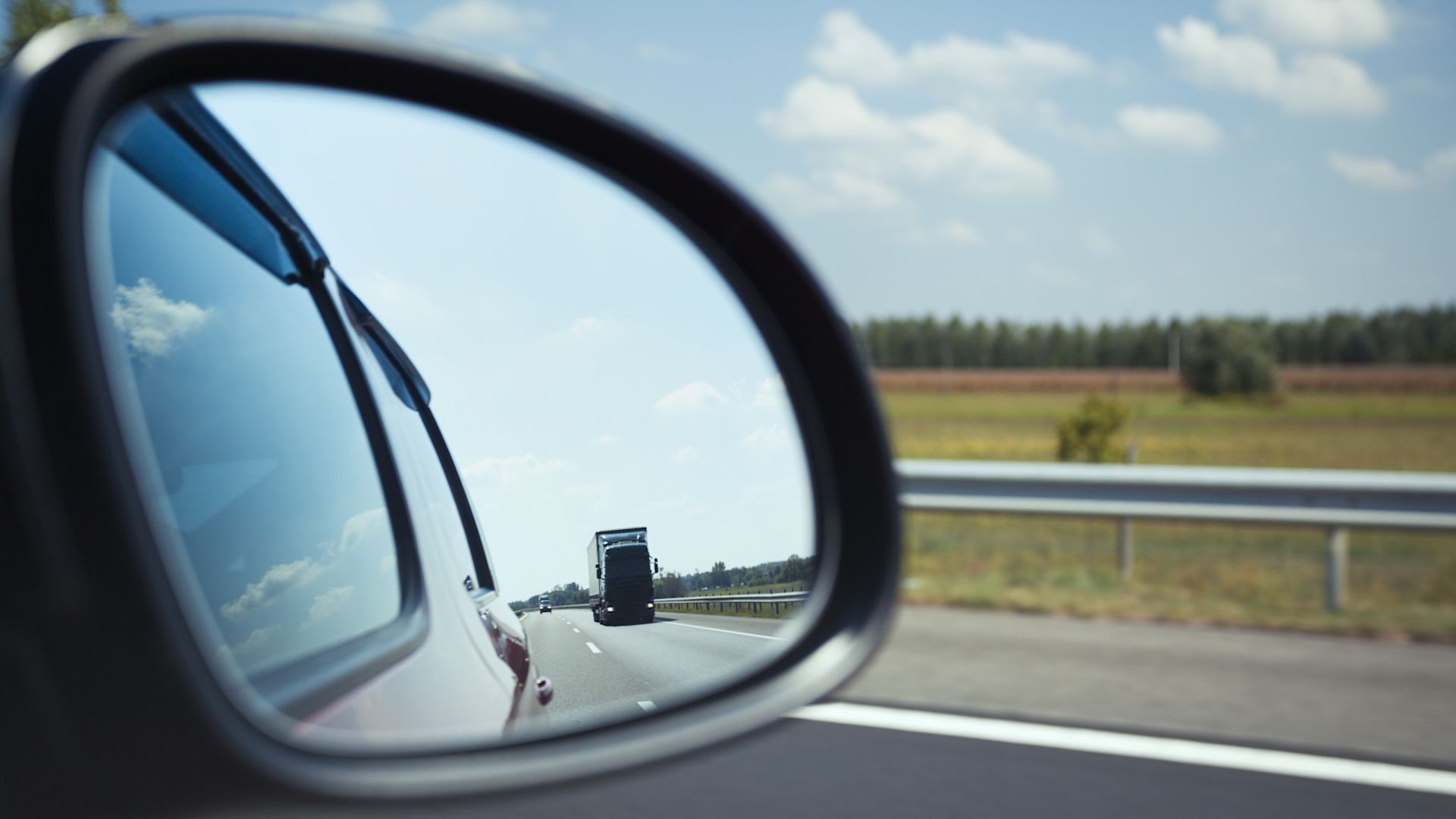 In der Spiegelung eines Seitenspiegels am Auto erscheint ein LKW.
