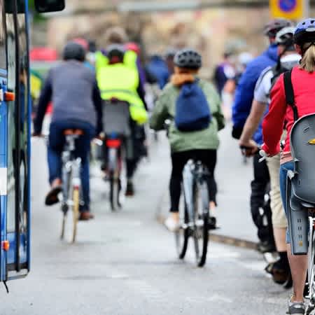 Das Bild zeigt viele Fahrradfahrer und Fahrradfahrerinnen parallel zu einem Bus eine Straße entlang fahren.