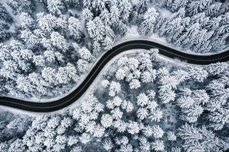 Straße im Winter, die durch verschneiten Wald führt, aus der Vogelperspektive.