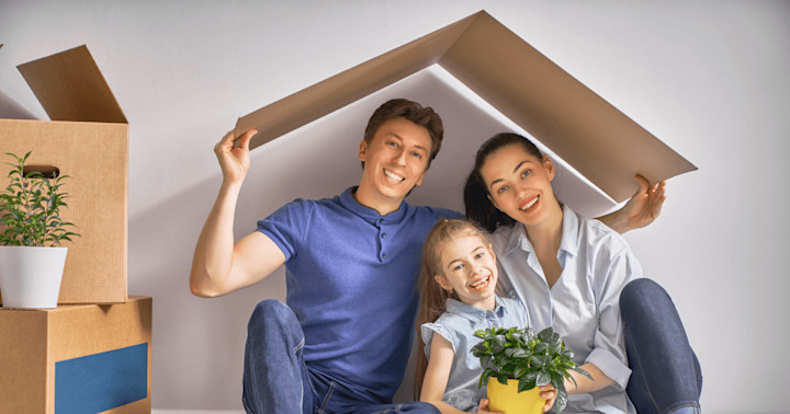 A family of three sitting on the floor in their house with a cardboard roof over their head. The roof signifies homeowners insurance coverage.