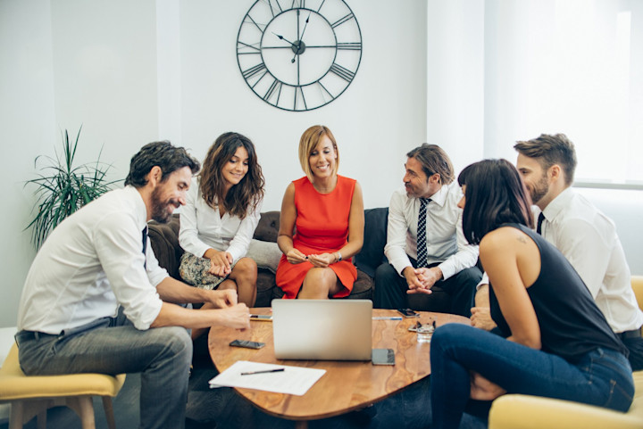A group of co-workers sitting around a coffee table looking at a laptop.