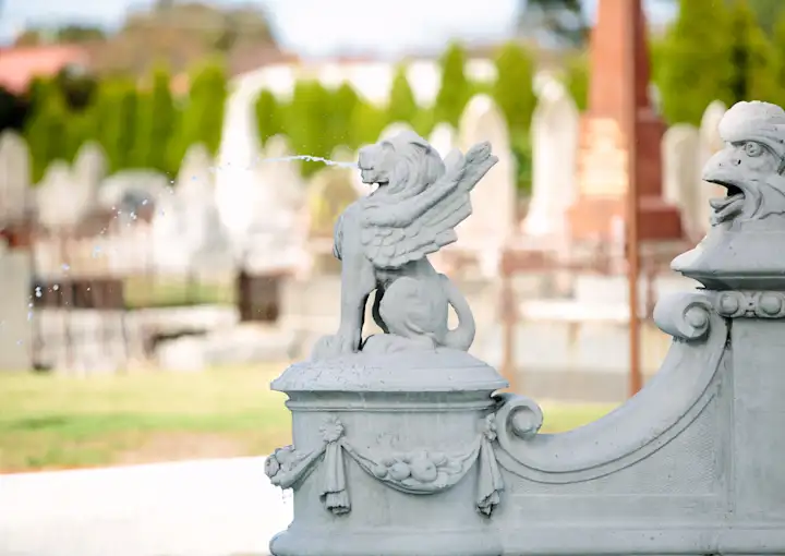 A watchful stone gargoyle sits on the historic fountain at Williamstown Cemetery