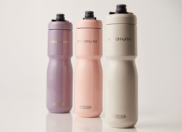 Three CamelBak Podium water bottles in mauve, peach, and cream colours with black sport caps on a neutral background.