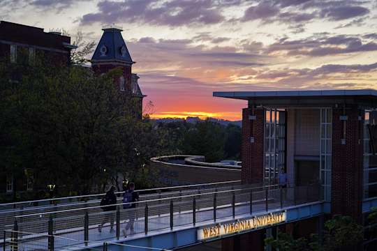 Two students walk across pedestrian bridge with sunset in the background