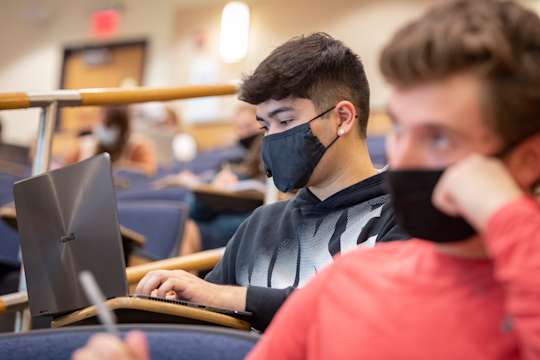 Student wearing mask types on laptop in classroom
