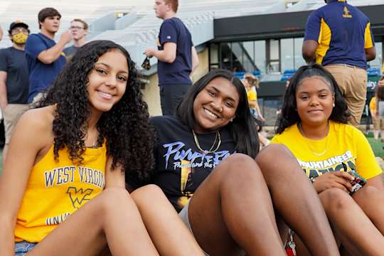 Three students smile during pre-event festivities on Mountaineer Field at the 2021 Sunday Night Lights.