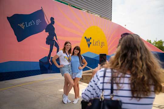 Two students getting their photo taken in front of the Let's Go mural.