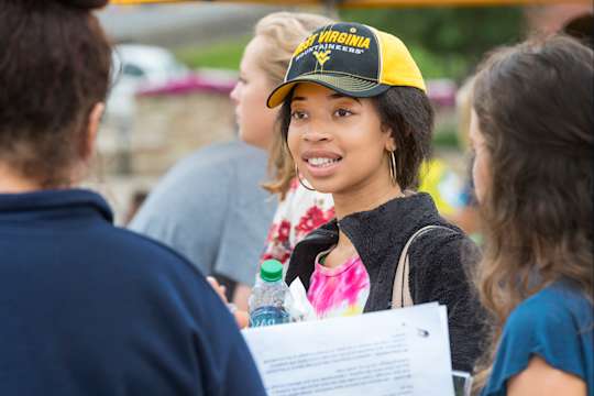 A student wearing a gold and blue West Virginia hat talks with other attendees at an event on the Mountainlair Plaza.
