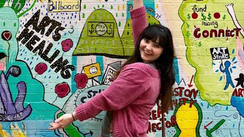Madison McGee poses in front of a colorful mural