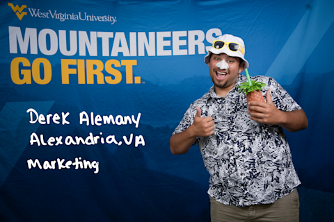 Derek Alemany, a Marketing major from Alexandria, VA, gives two thumbs up. He's wearing a white bucket hat and sunglasses and is carrying a pineapple-shaped drink container.