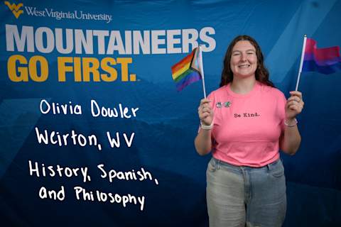 Olivia Dowler, a History, Spanish and Philosophy major from Weirton, WV, wears a pink "Be Kind" T-shirt and holds Progress Pride and Bisexual Pride flags.