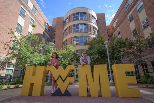 Two students pose with the Flying WV logo and giant HOME letters outside Honors Hall