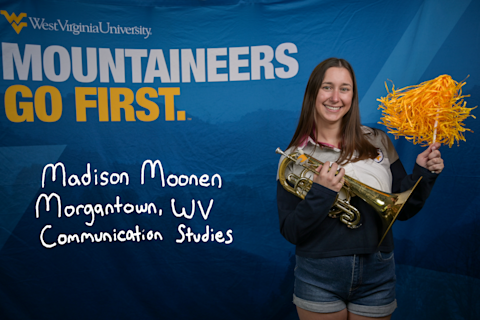 Madison Moonen, a Communication Studies major from Morgantown, WV, holds a gold pom pom in one hand and a horn in the other.
